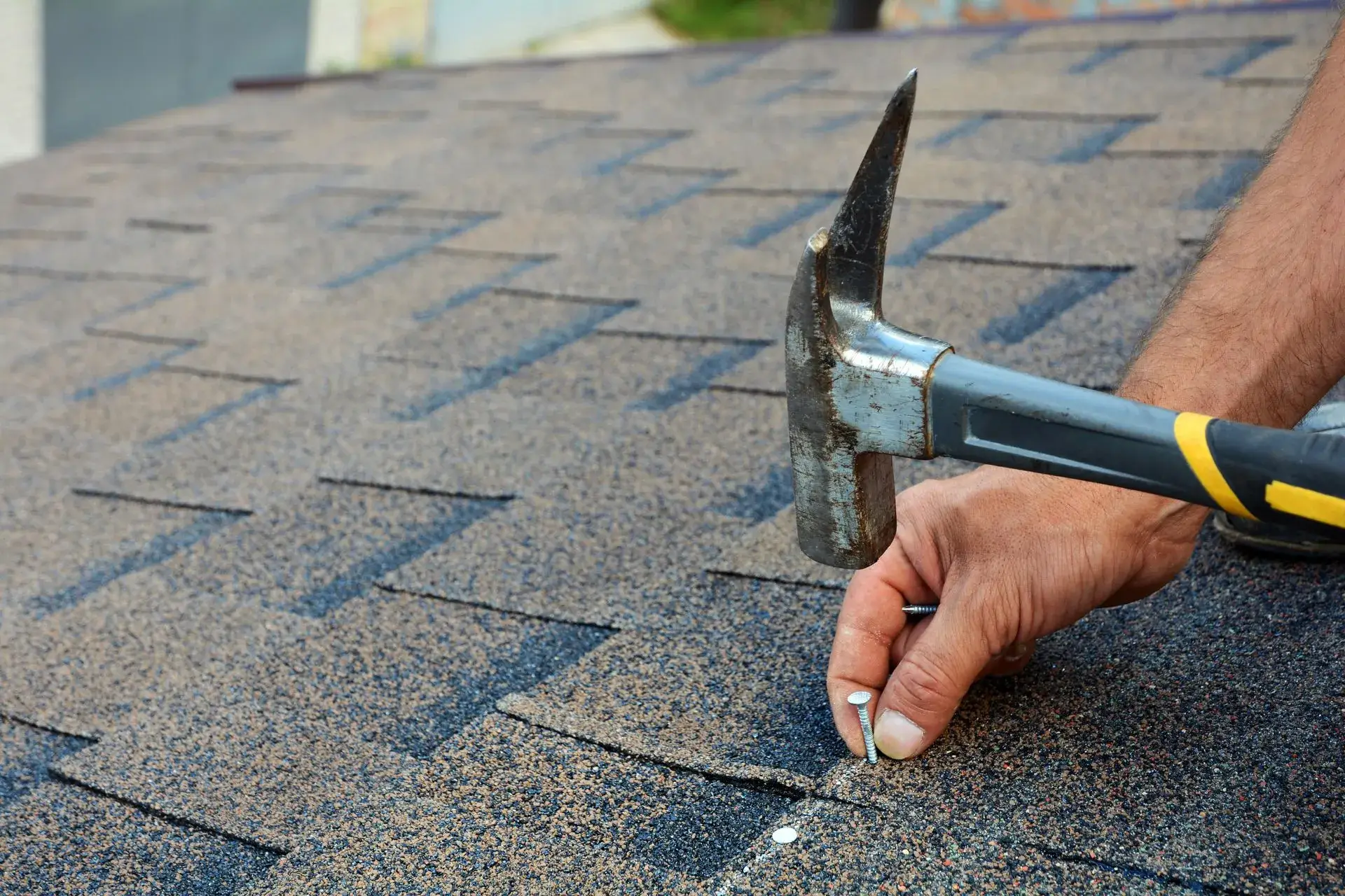 Roofer driving a nail into a shingle