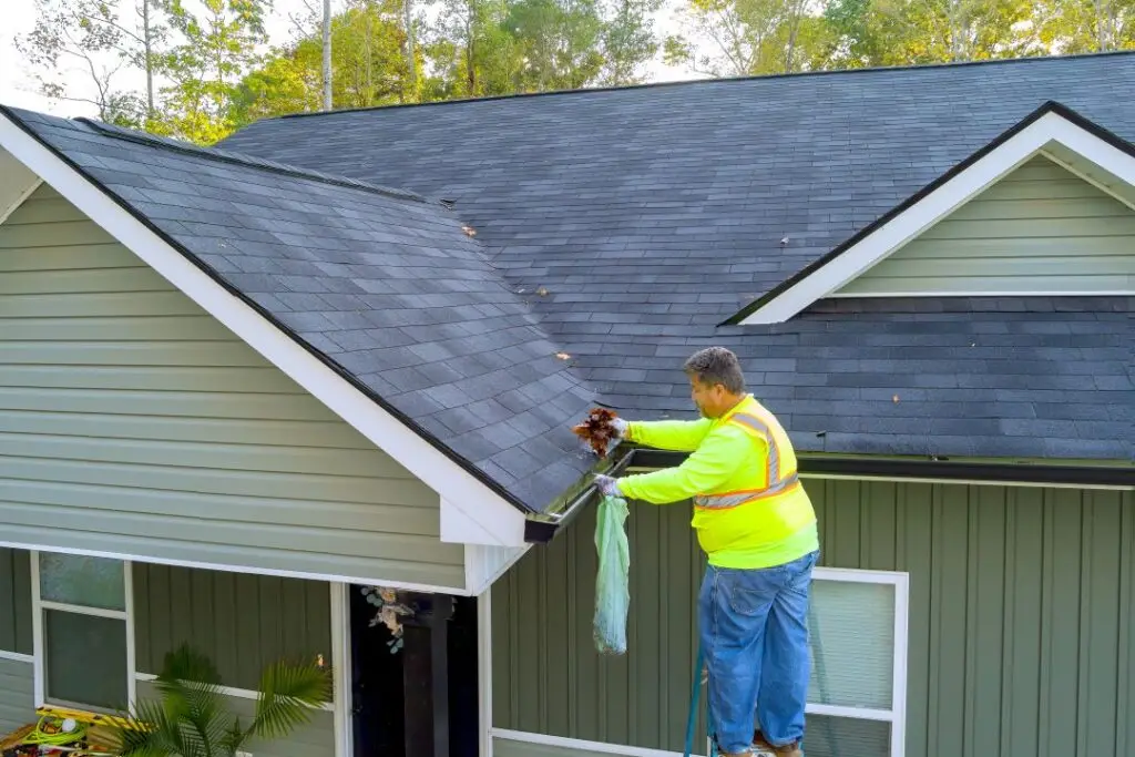 worker-is-cleaning-clogged-roof-gutter-from-dirt