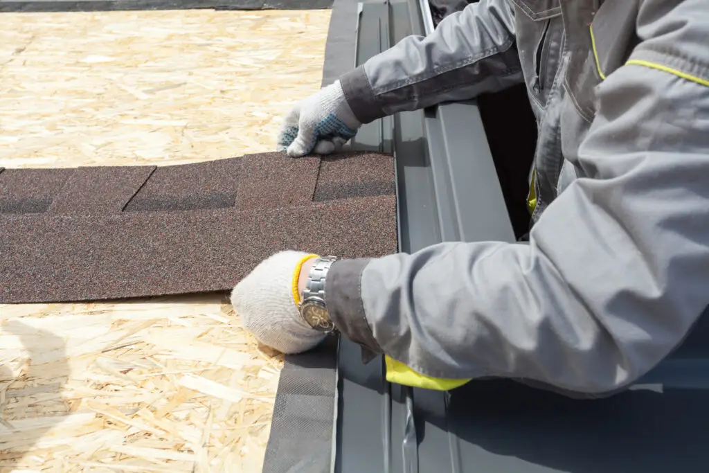 Roof replacement materials - A male contractor laying down asphalt shingle sheets on a home's roof.