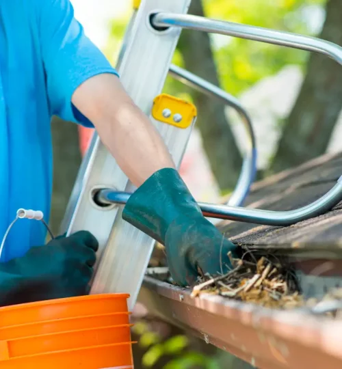 Avoiding roof problems - A man removing dried leaves from a home's gutter.