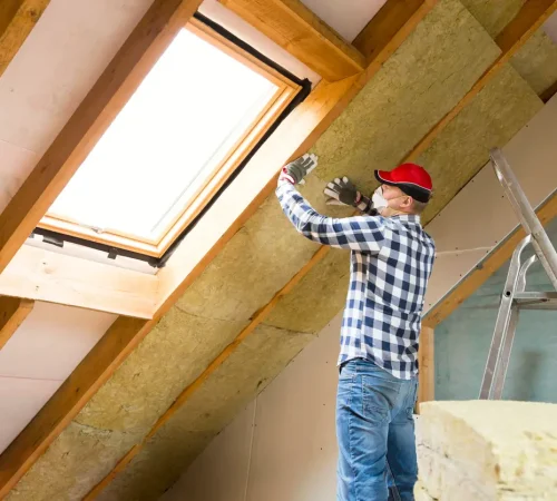 Preventing roof heat damage - A male contractor installing an insulator on a home's attic.